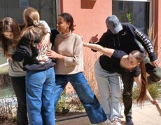 Schülerinnen und Schüler bei einem Teambuilding Spiel. Halten einander fest, stehen auf einem Blatt Papier zu zweit.
