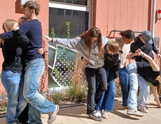 Schülerinnen und Schüler bei einem Teambuilding Spiel. Halten einander fest, stehen auf einem Blatt Papier zu zweit.