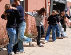 Schülerinnen und Schüler bei einem Teambuilding Spiel. Halten einander fest, stehen auf einem Blatt Papier zu zweit.